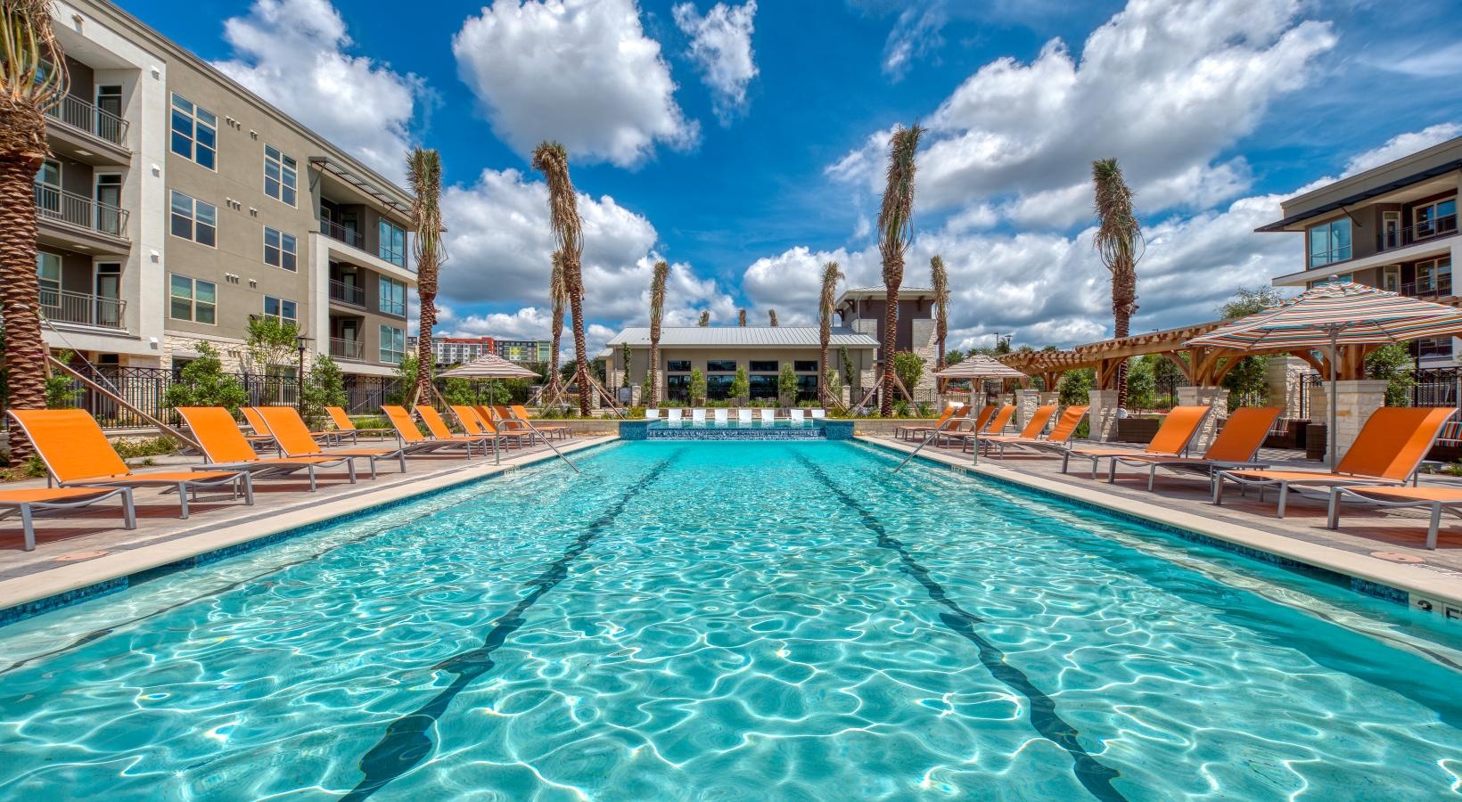 Shimmering resort-style pool a swimming pool with lounge chairs and a building in the background
